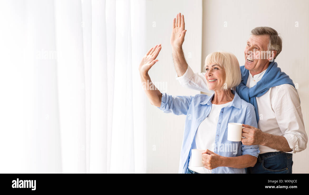 Happy senior couple looking through window and hugging Stock Photo
