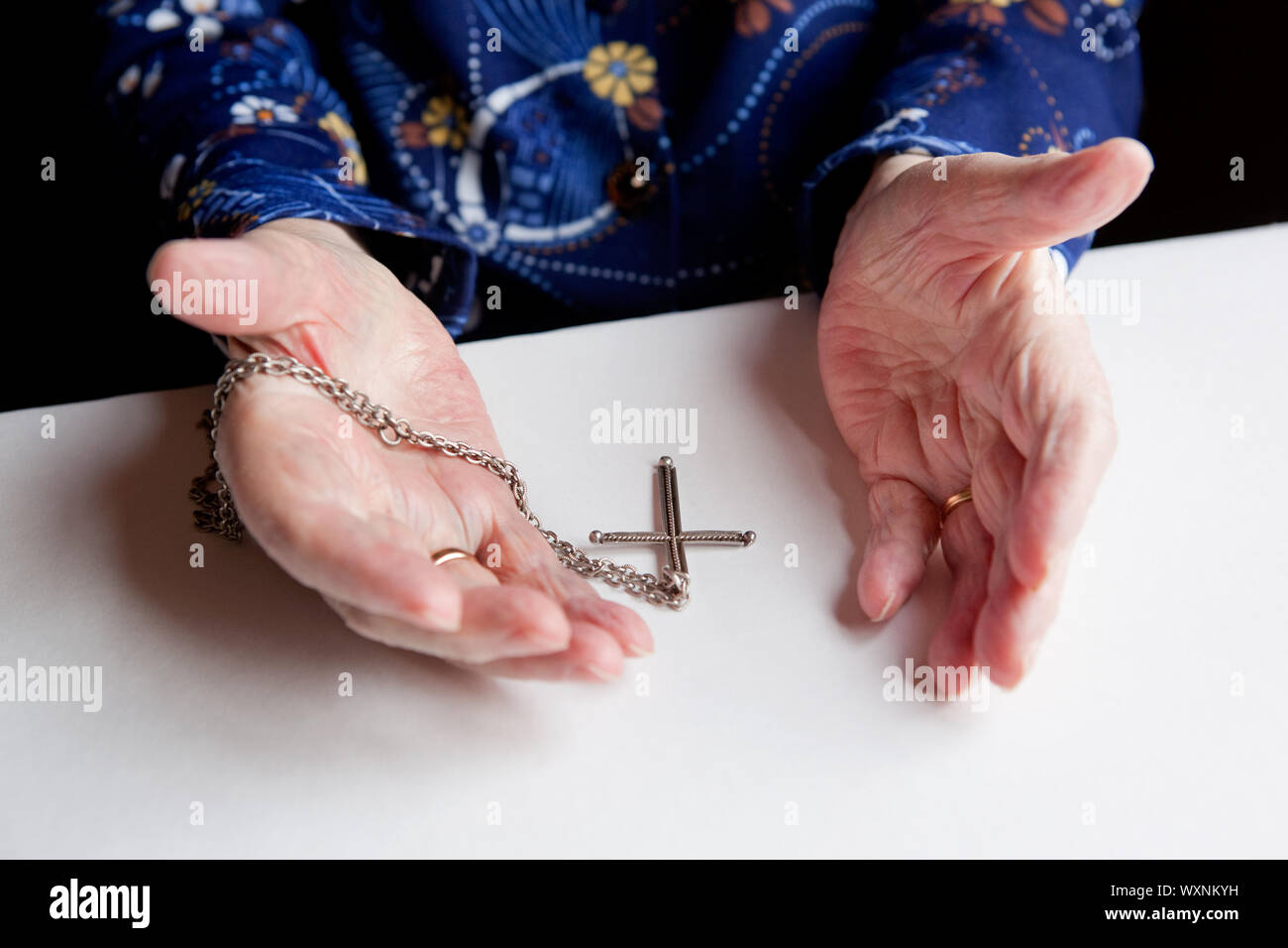 A pair of old hands and a cross - shallow depth of field with focus on the cross Stock Photo