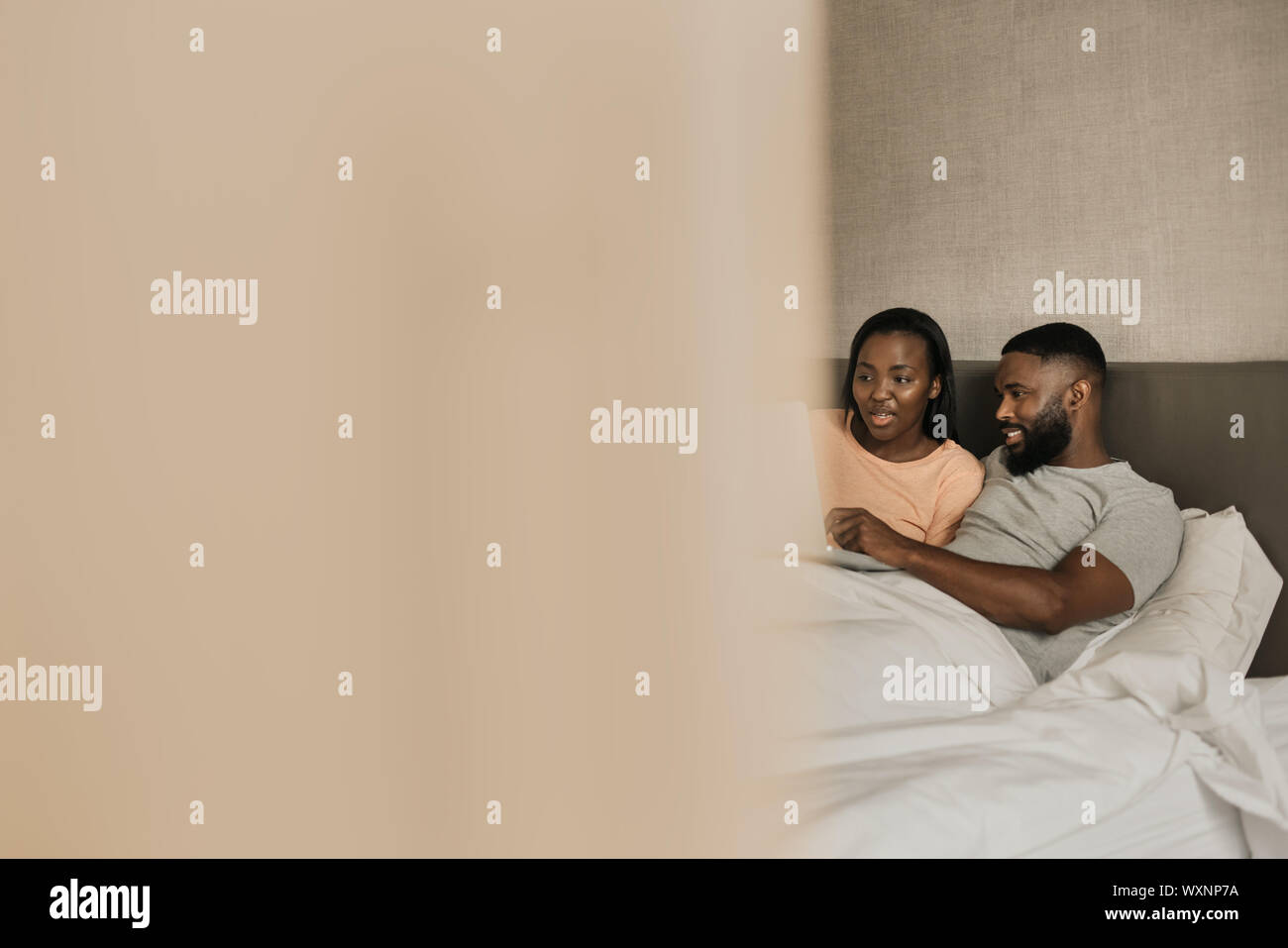 Smiling African American couple lying in bed using a laptop Stock Photo ...