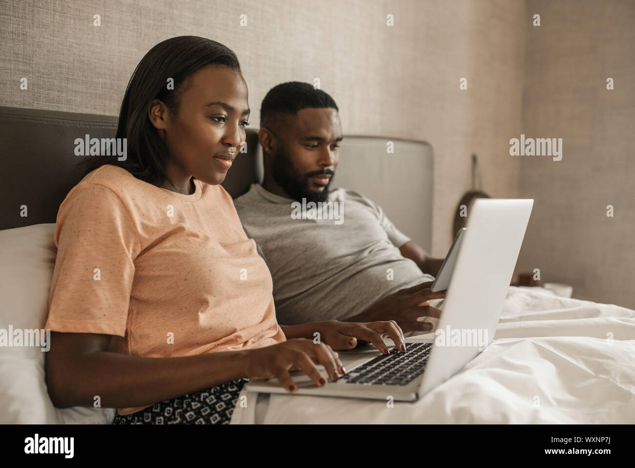 Smiling African American couple lying in bed checking their social ...