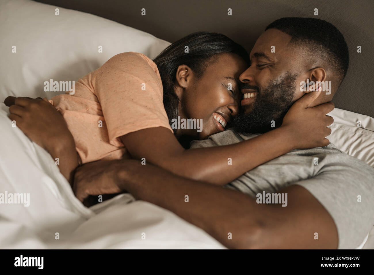 Affectionate young African American couple hugging each other in bed ...