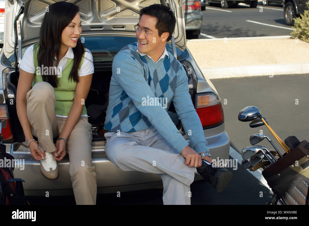 Couple Sitting on Rear Bumper of Car Putting on Golf Shoes Stock Photo