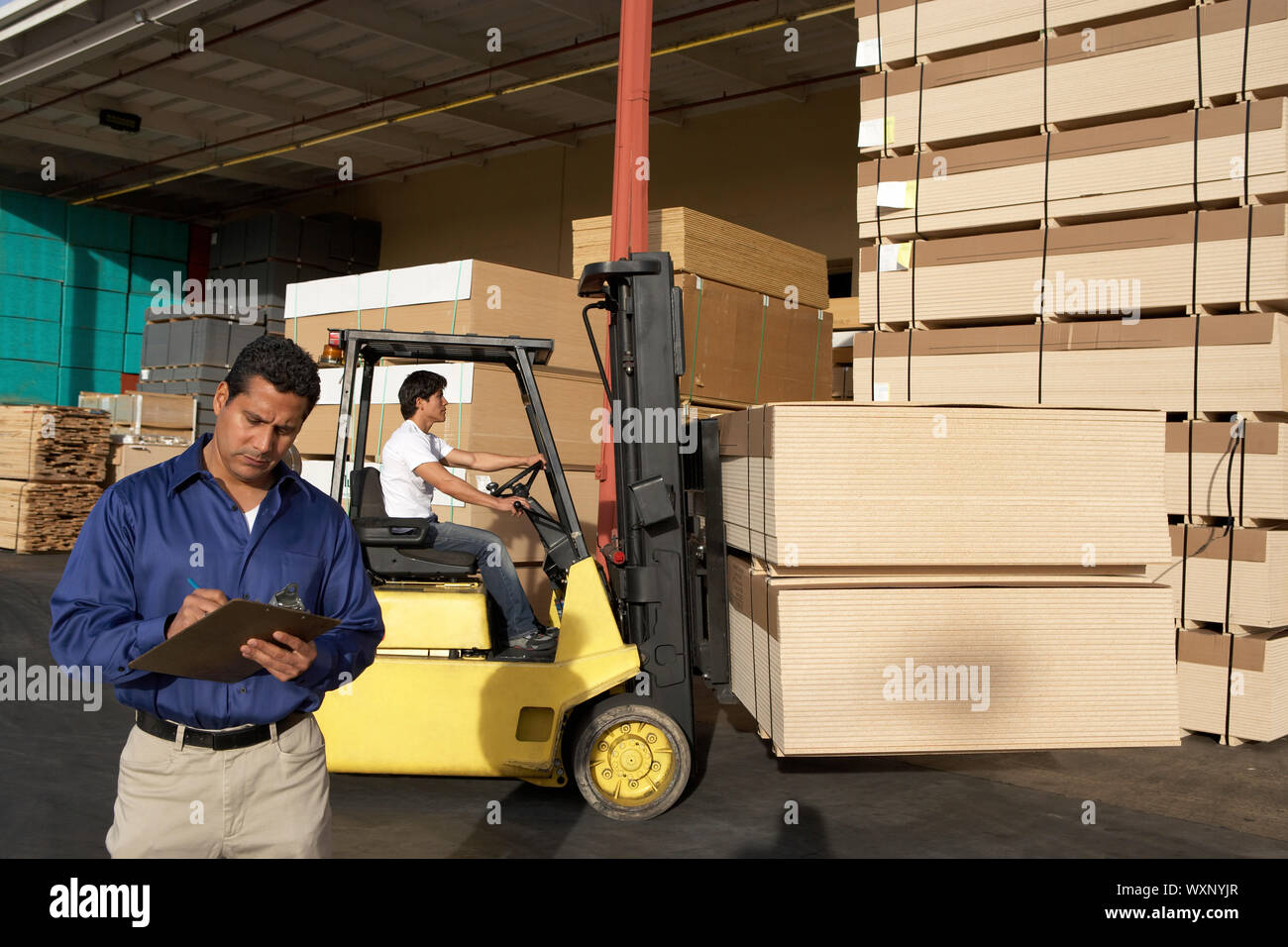 Manager Holding Clipboard on Loading Dock of Lumber Warehouse Stock
