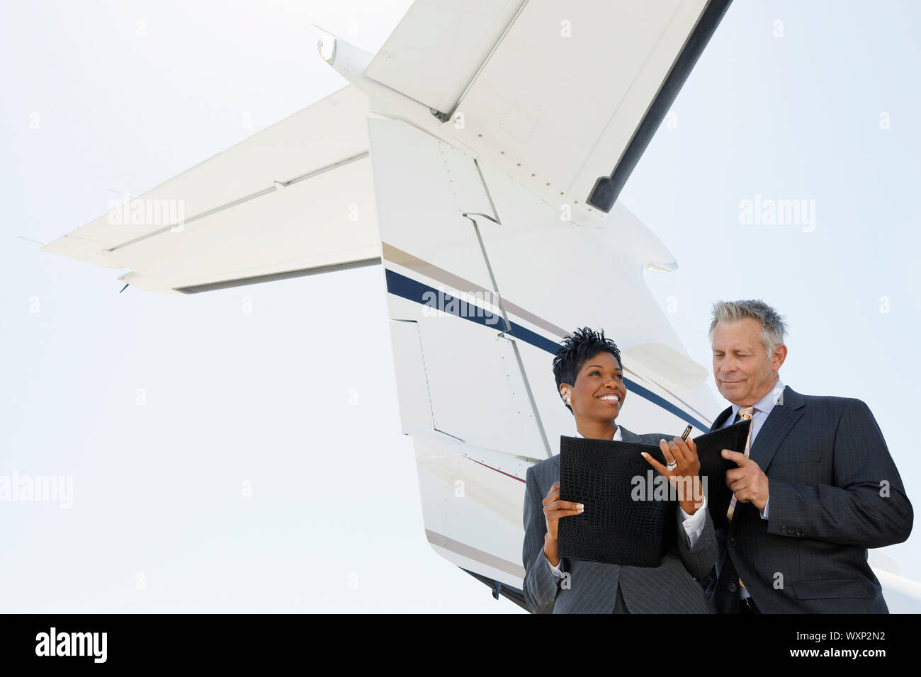 Confident multiethnic business people discussing below wing of private jet Stock Photo