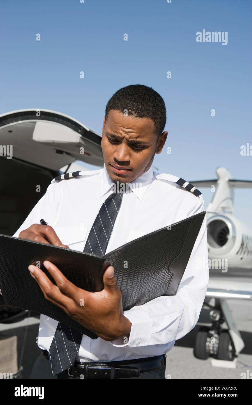 Airline pilot standing and making notes in front of airplane Stock