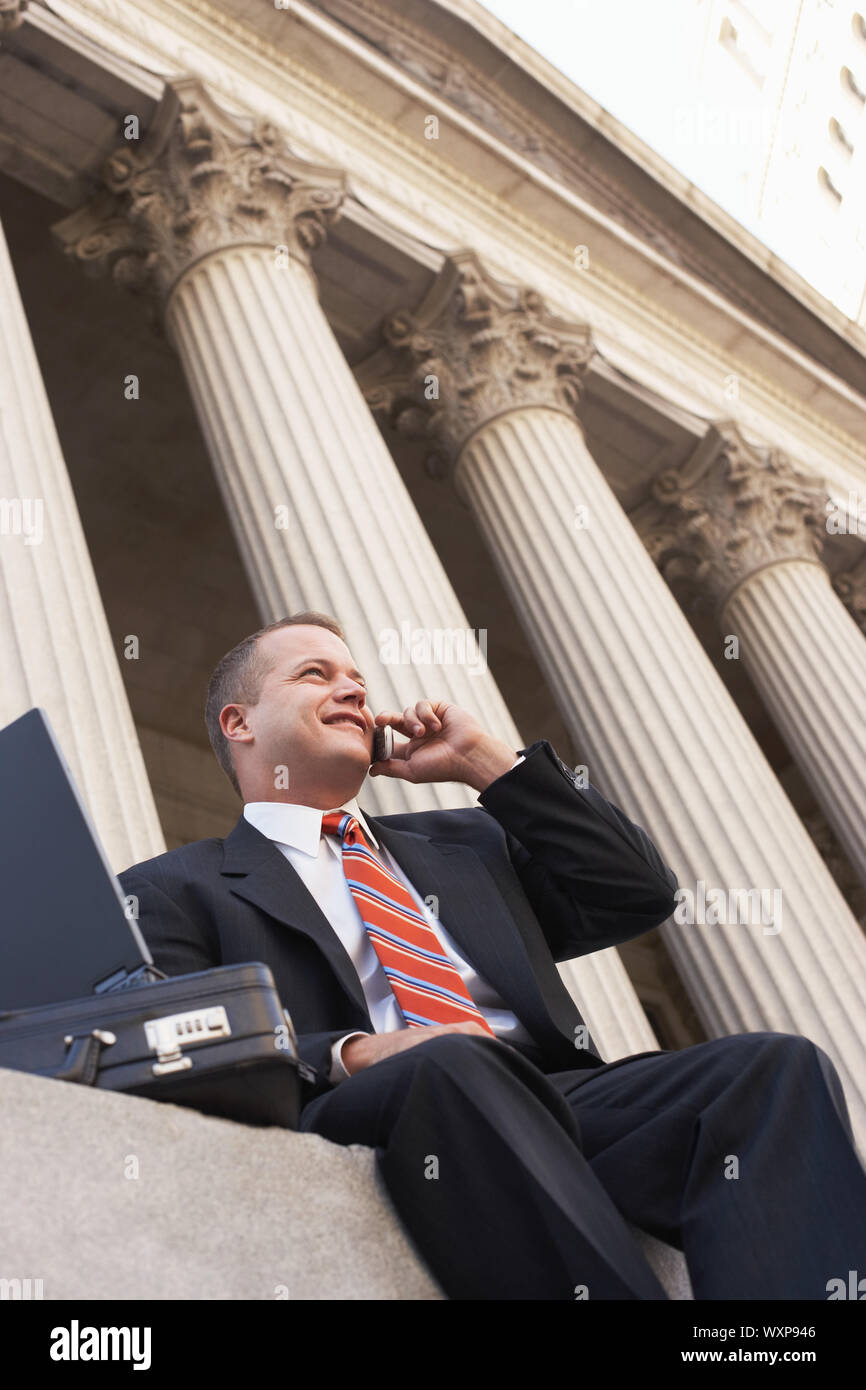 Low angle view of happy businessman using cell phone in front of building Stock Photo