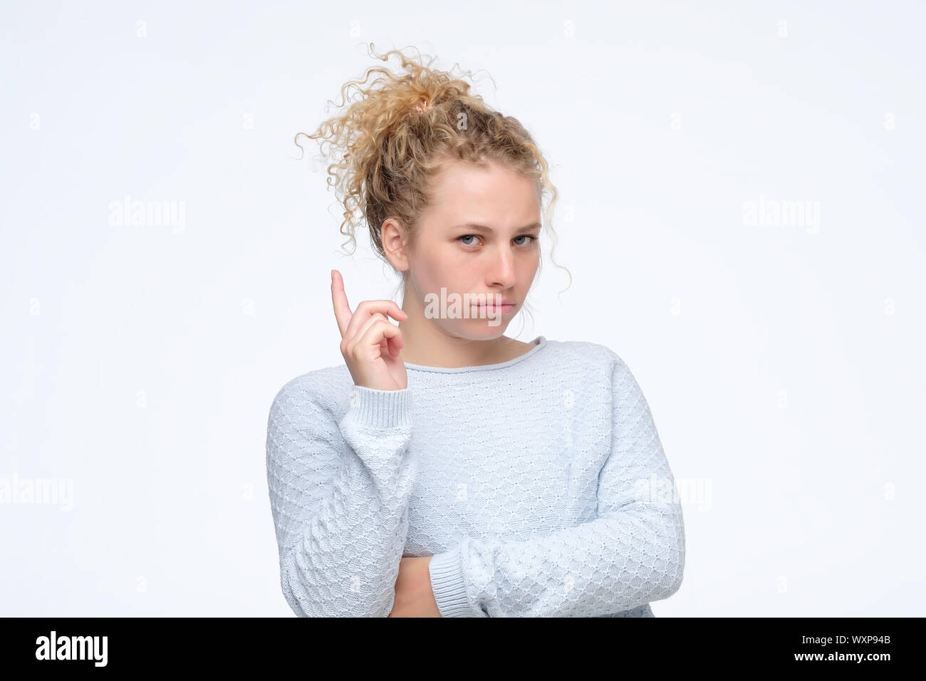 Young caucasian blonde girl showing the index finger up giving advice. Studio shot Stock Photo