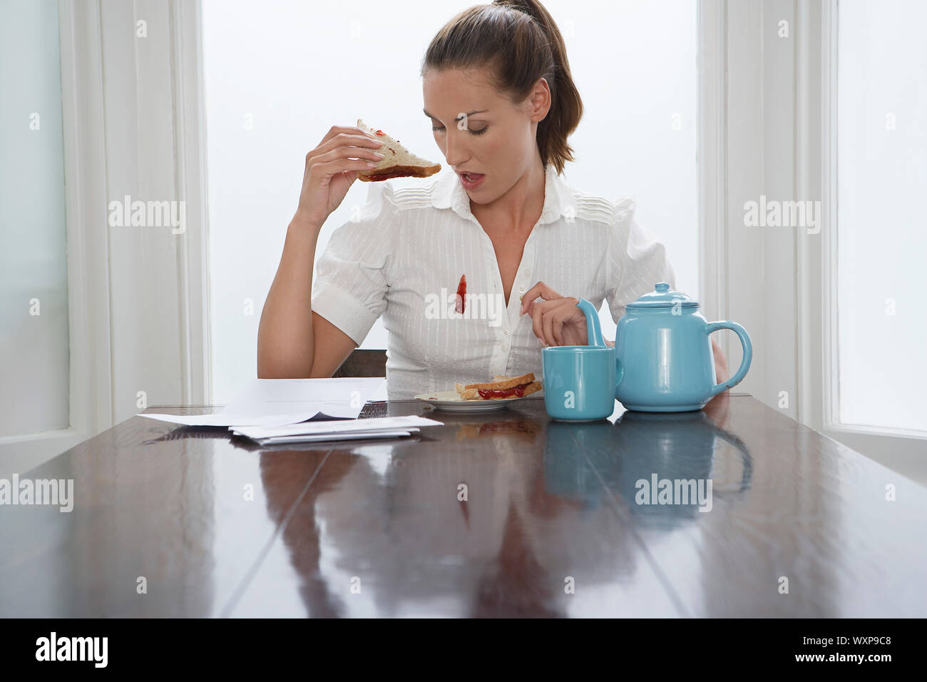Beautiful woman looking at stain on shirt while having breakfast Stock Photo
