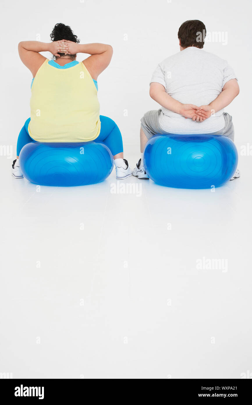 Rear view of an overweight man and woman exercising on exercise balls Stock Photo