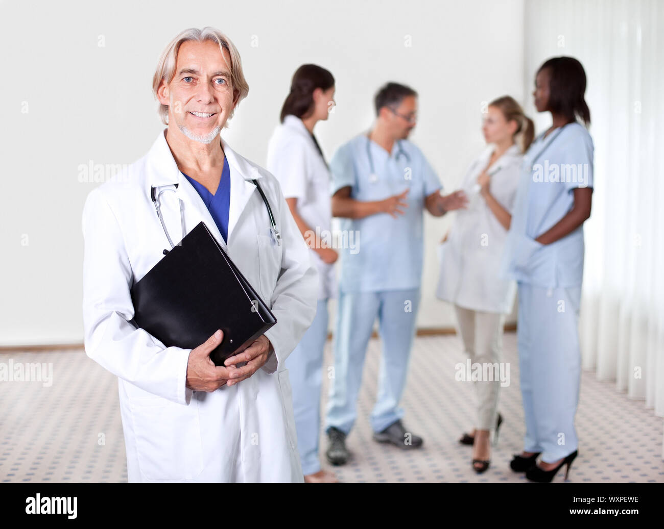 Mature doctor holding files with a group of doctors discussing behind