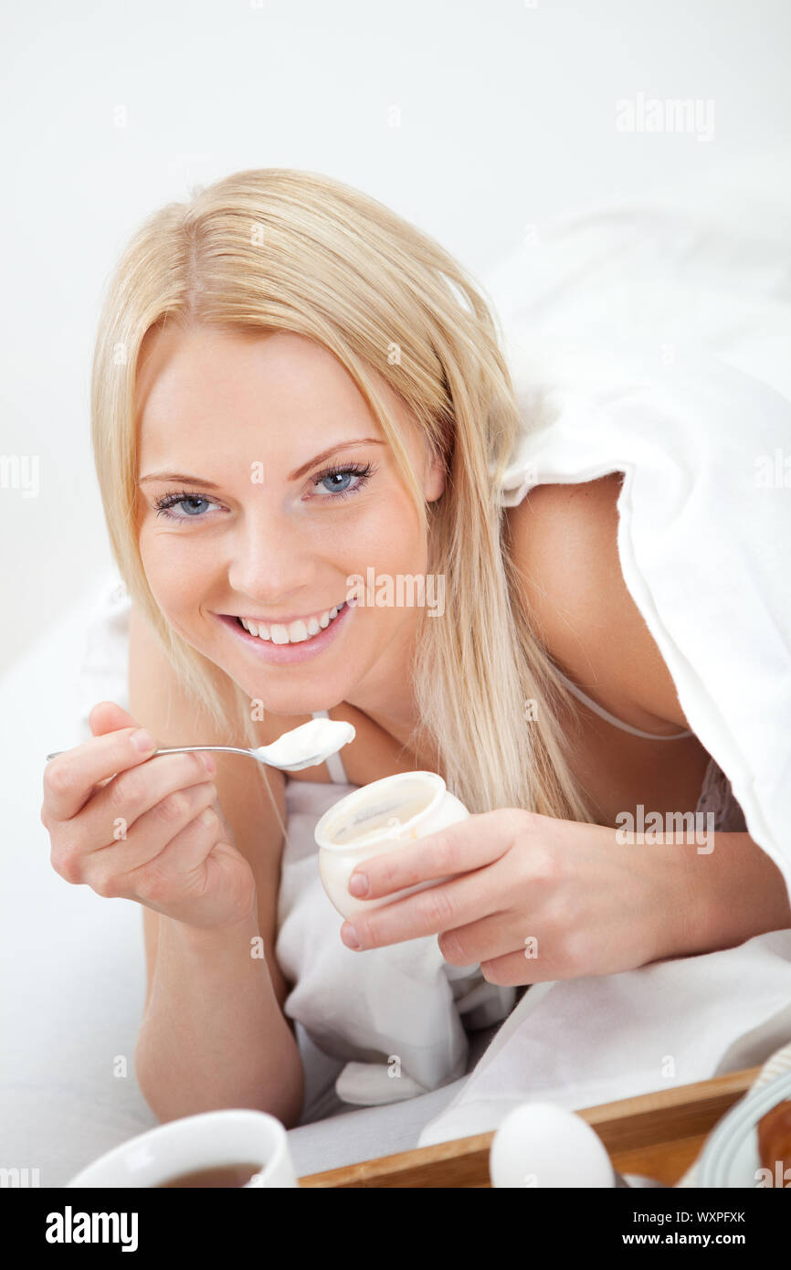 Beautiful woman eating yogurt in bed during the breakfast Stock Photo
