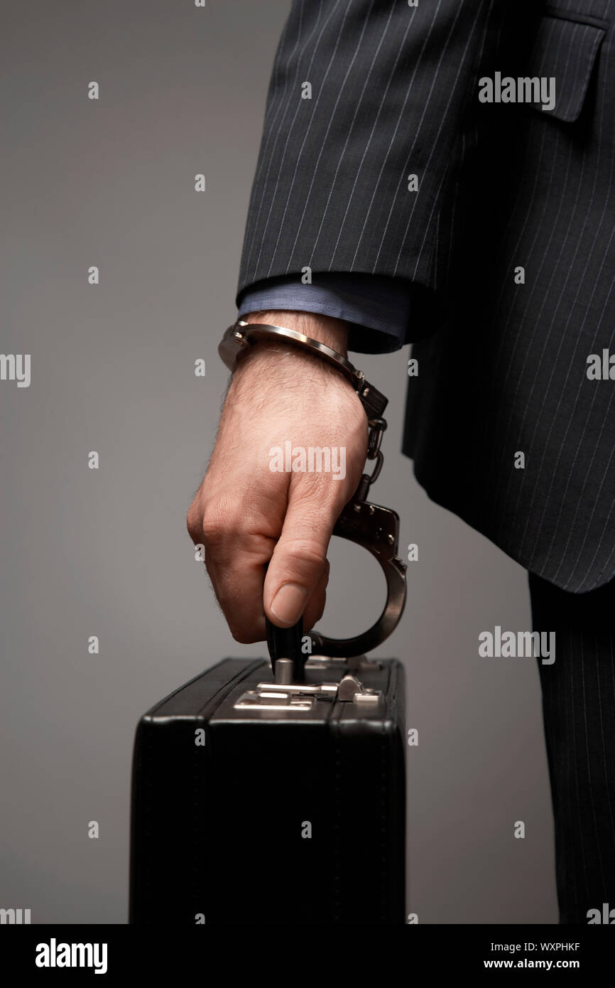 Briefcase handcuffed to businessman's wrist over colored background