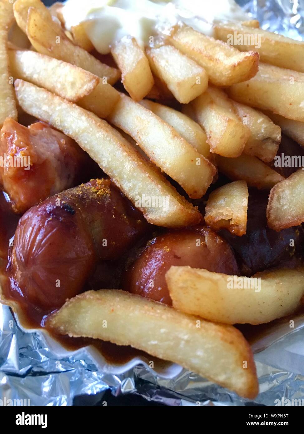 Currywurst & Pommes: Famous German Fast Food (Curry Sausage with French Fries and Curry Sauce) with ketchup and mayonaise on aluminium foil Stock Photo