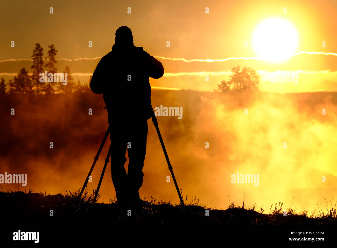 Photographer with tripod and camera taking photographs of sunrise or ...
