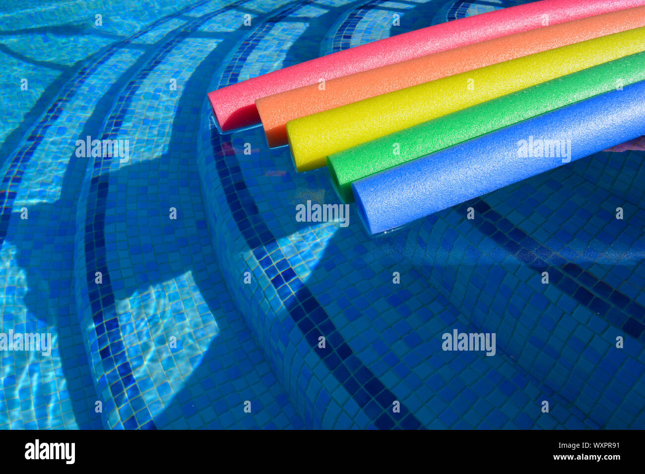 Rainbow coloured pool noodles floating in a swimming pool, summer fun