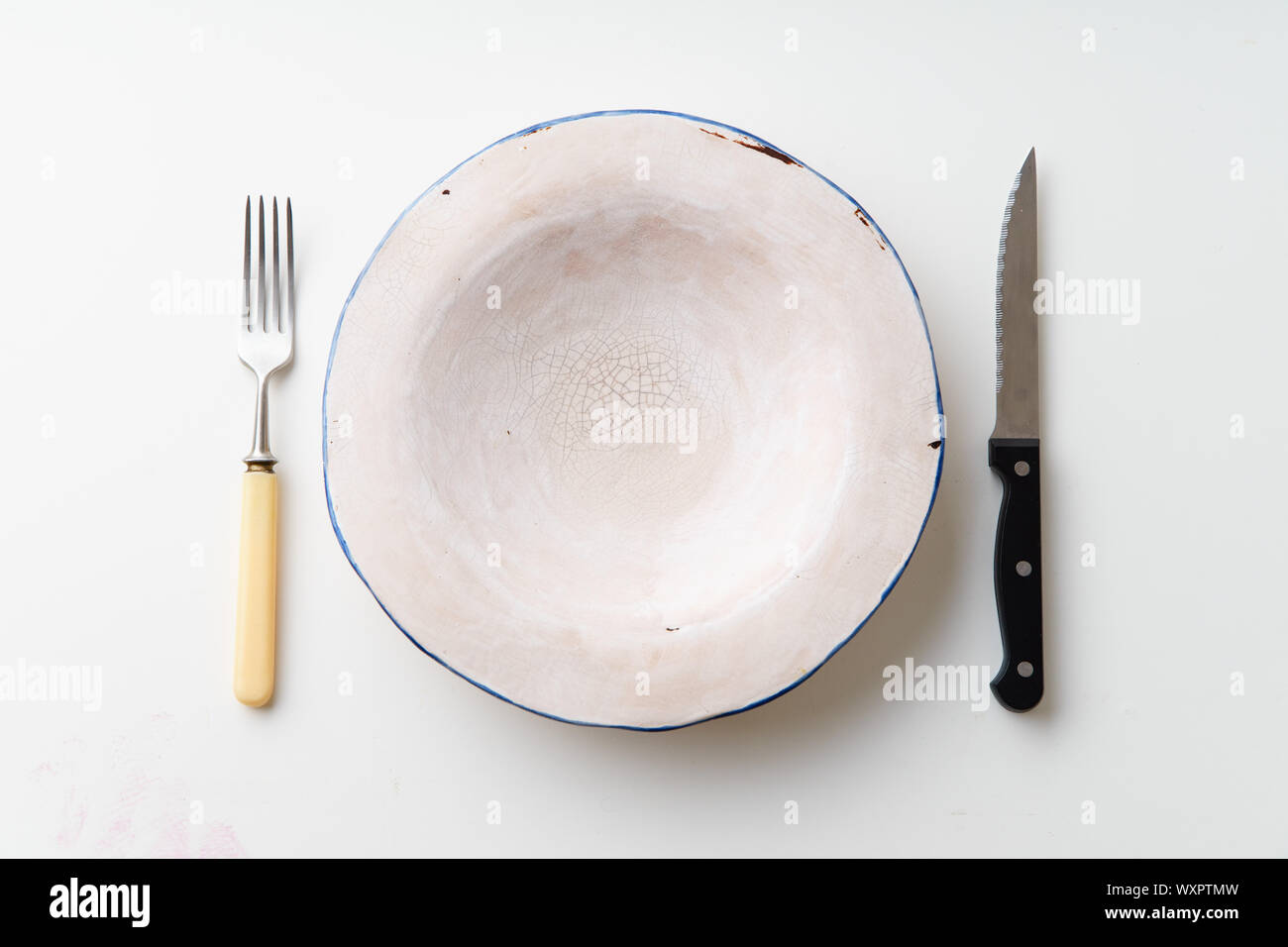 Handmade ceramic empty plate with knife and fork on white background Stock Photo