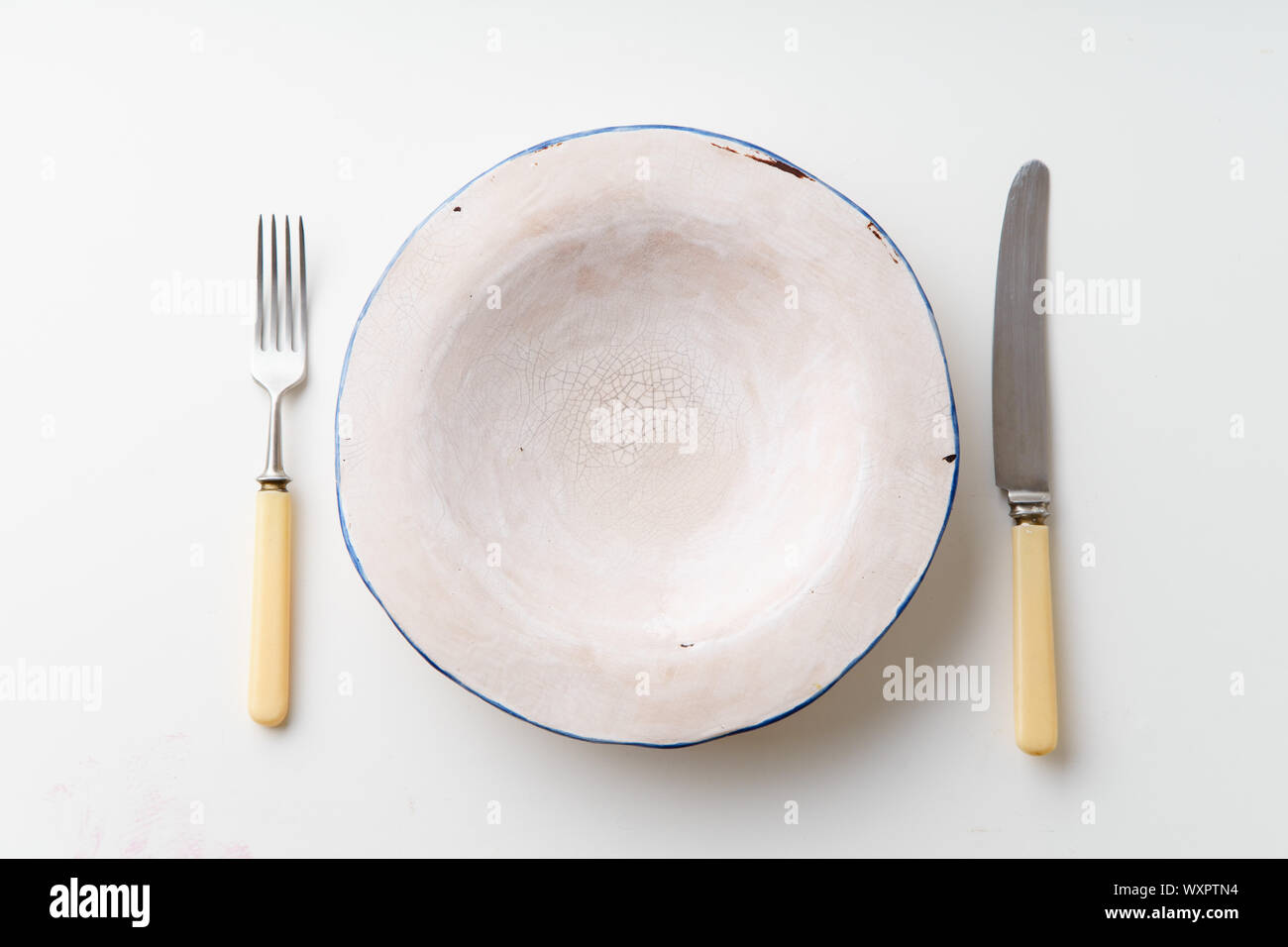 Handmade ceramic empty plate with knife and fork on white background Stock Photo