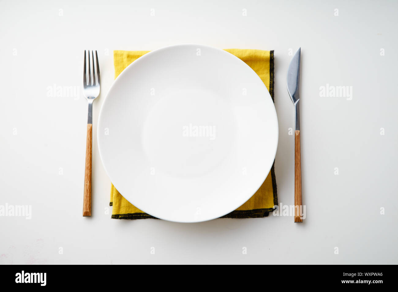 White empty plate with knife and fork and yellow textile napkin on ...