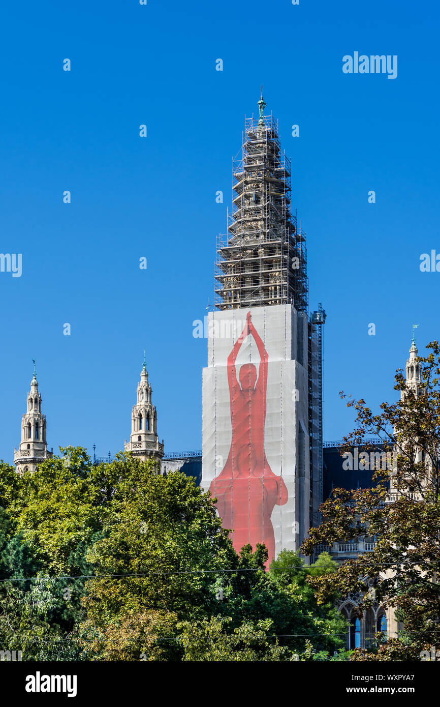 Town Hall (Rathaus) tower encased in scaffolding (2019) and protective sheeting with yoga illustration - Vienna, Austria. Stock Photo