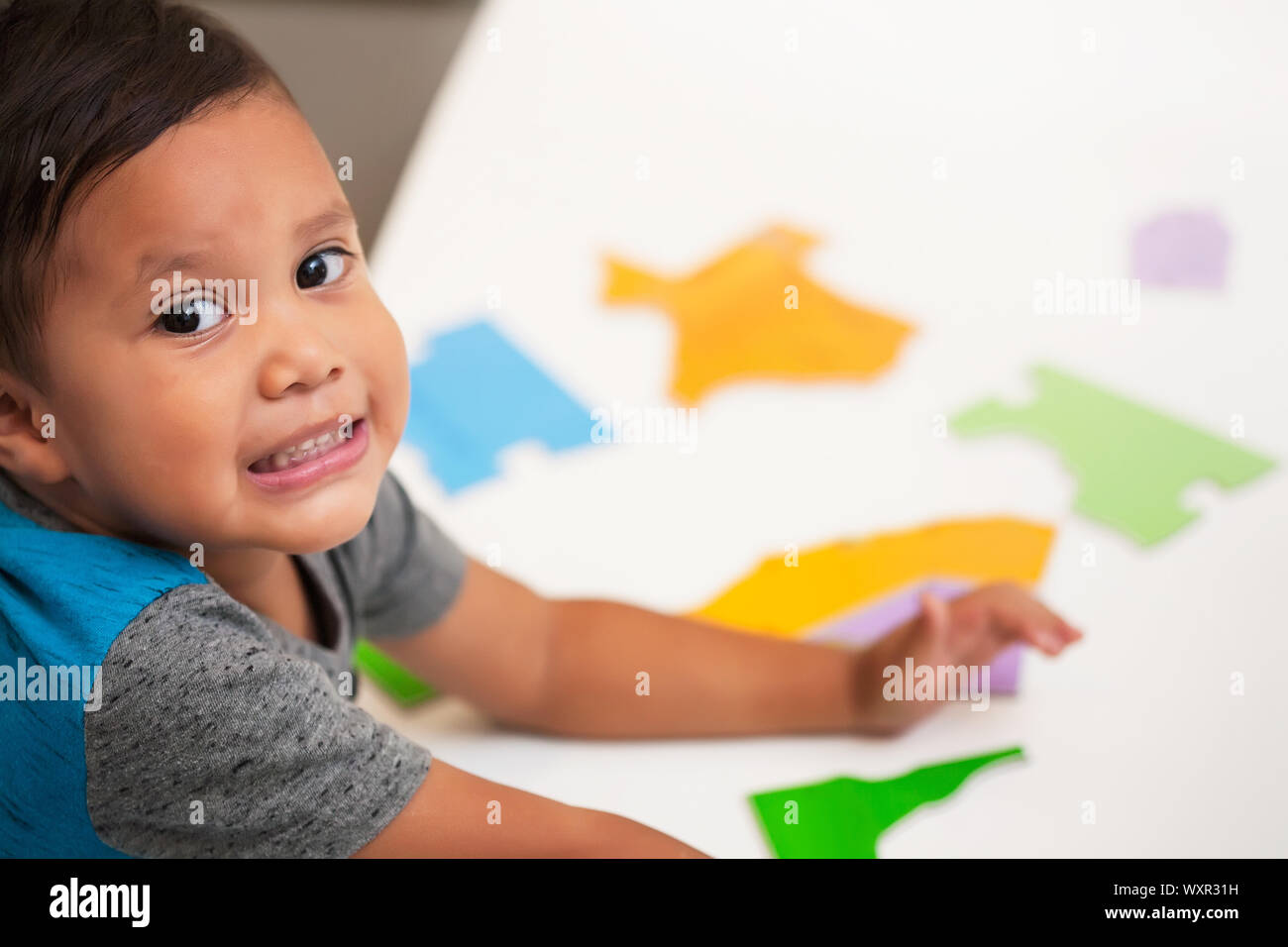 A preschool age young boy  having fun and smiling while playing with manipulative toys on a white table. Stock Photo