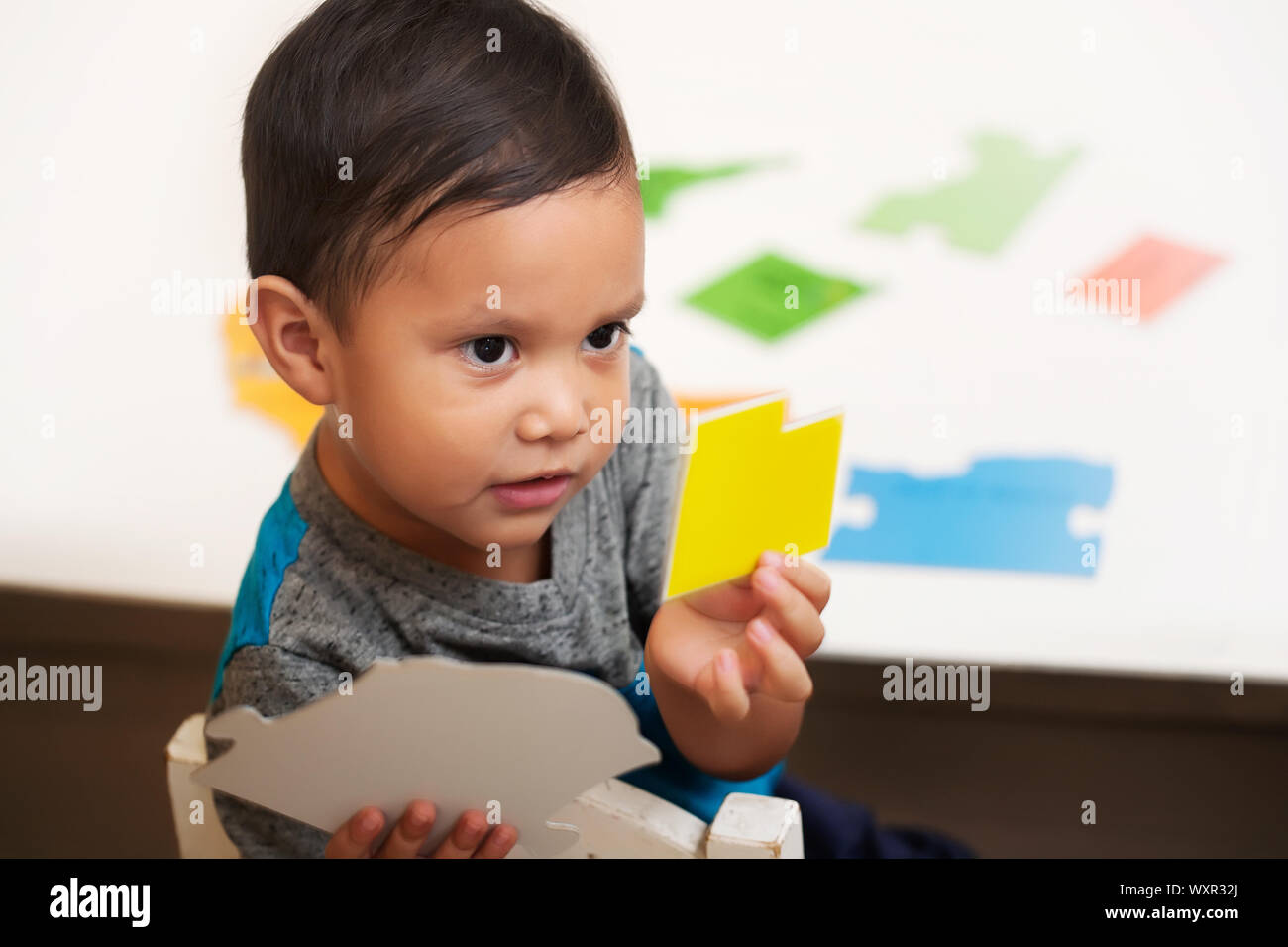 A smart latino boy choosing the correct colored shape from a table and showing it to the preschool teacher. Stock Photo