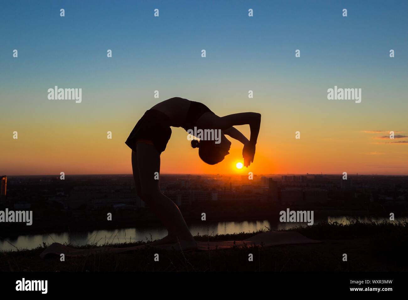 Silhouette of sporty woman practicing yoga in the park at sunset - drop ...