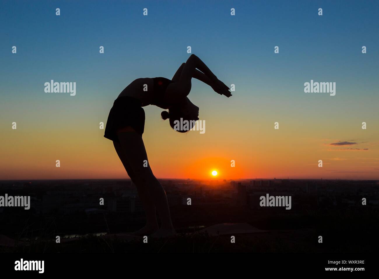 Silhouette of sporty woman practicing yoga in the park at sunset - drop ...