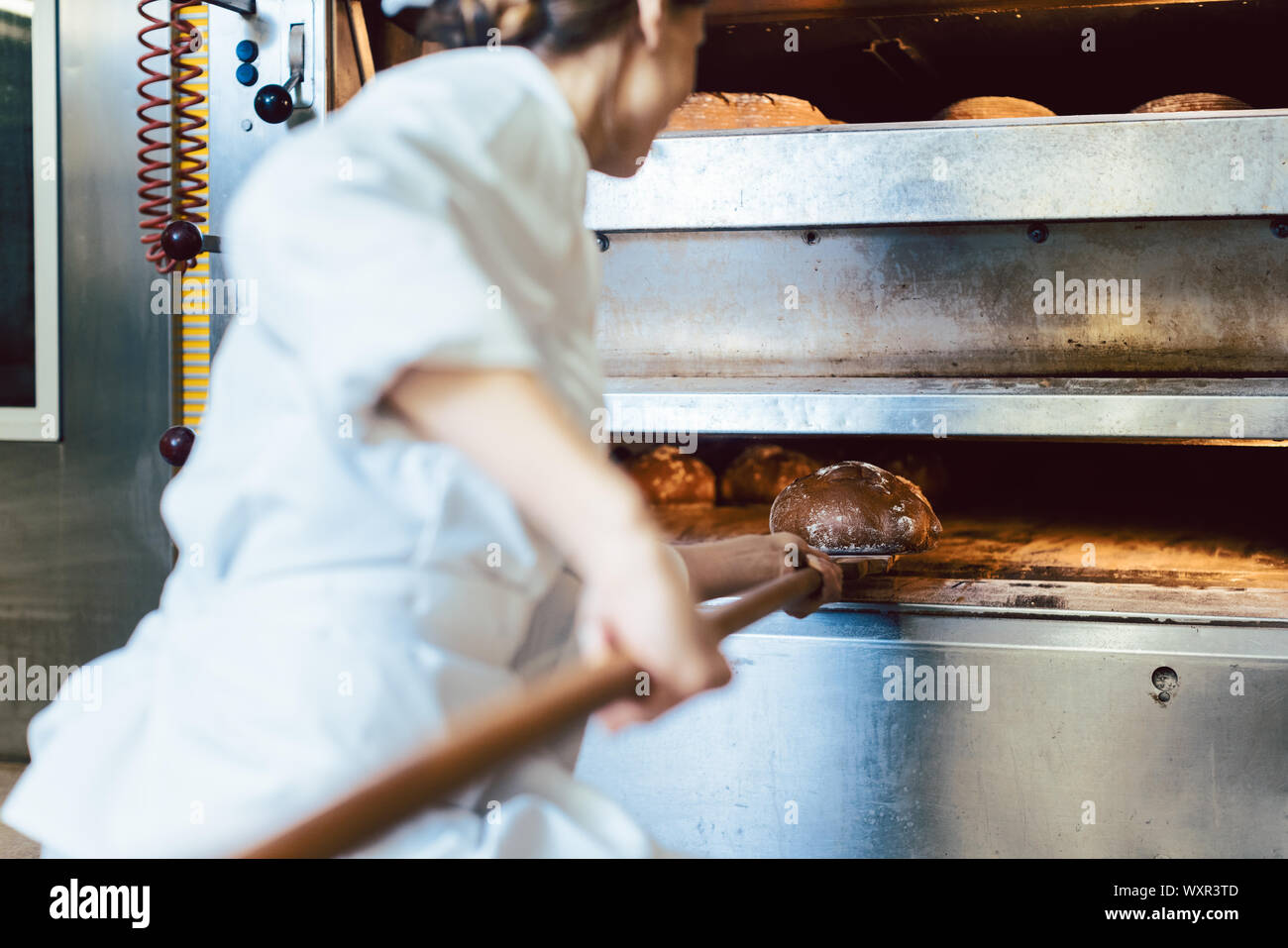 Baker putting bread in the bakery oven cowering on the floor of the bakery Stock Photo