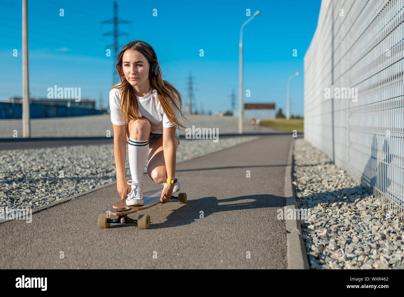 stylish girl in white stockings ride on longboard down the street and ...