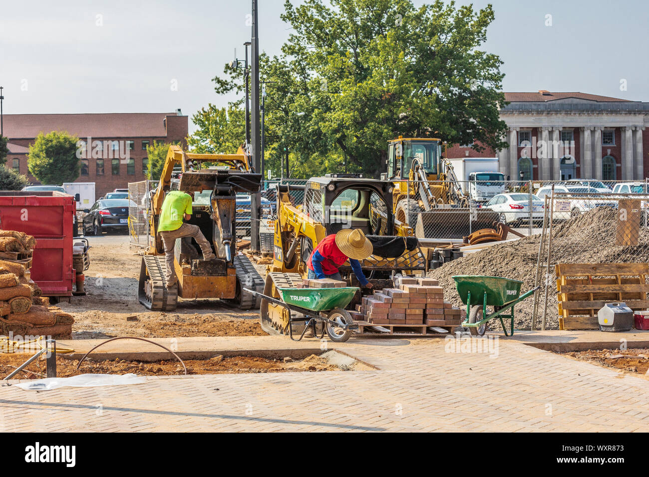 HICKORY, NC, USA-13 SEPT 2019: Construction scene, with driver climbing onto front loader and worker stacking bricks into a wheelbarrow Stock Photo