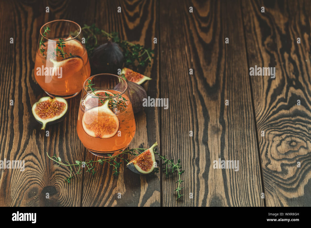 Pink cocktail with fig, thyme and ice in glass on dark wooden background, close up. Summer drinks and alcoholic cocktails. Alcoholic or detox cocktail Stock Photo