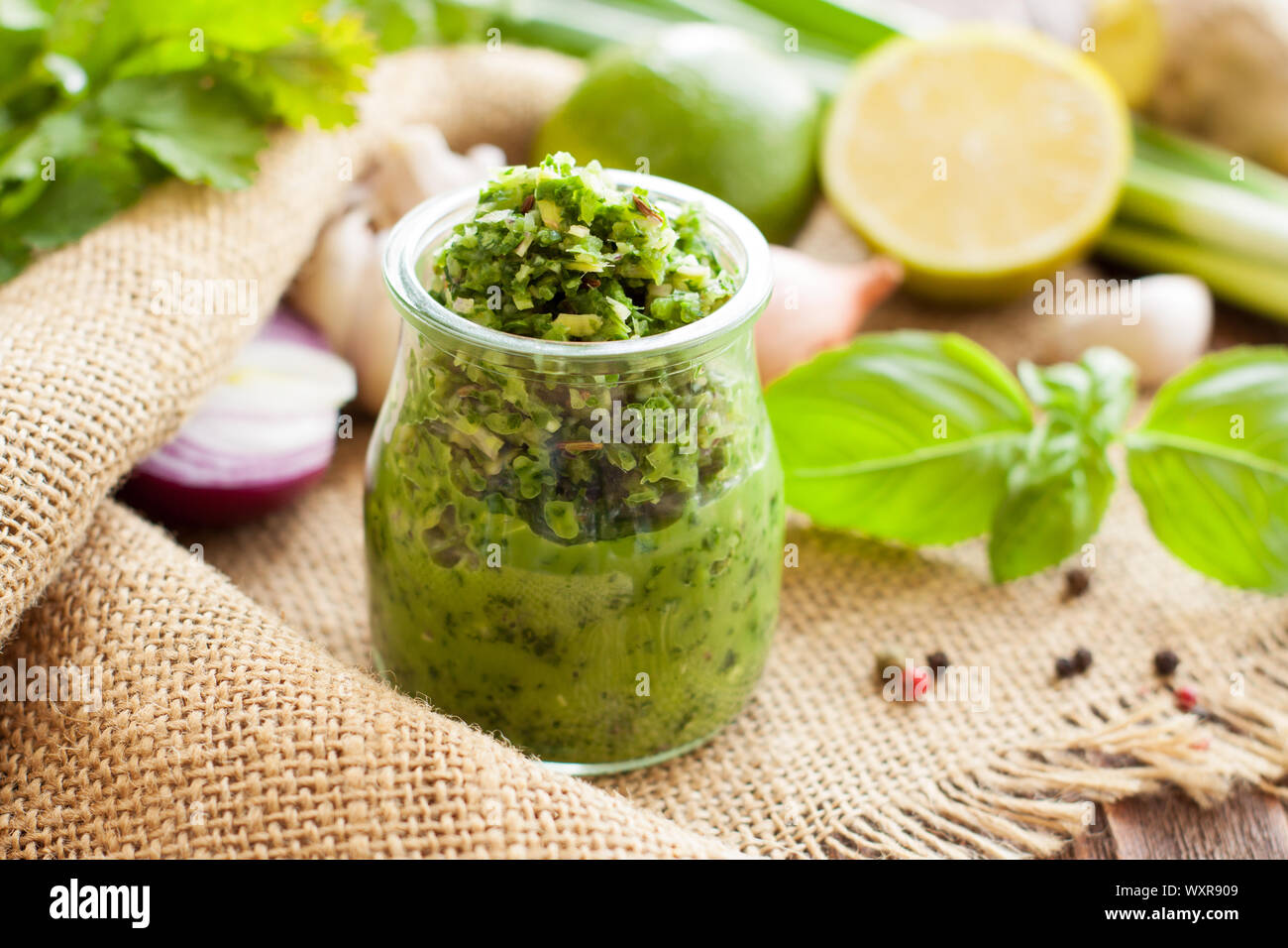 Green sauce in a glass jar in background with basil, lime, onion and parsley. Thai green curry paste Stock Photo