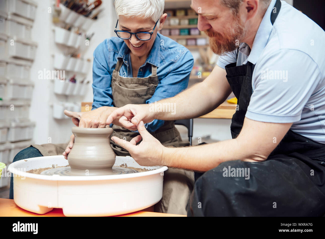 Senior woman spinning clay on a wheel with a help of a teacher at