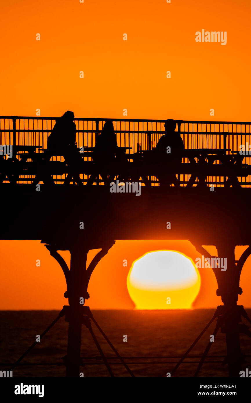 Aberystwyth Wales UK, Tuesday 17 September 2019 People having a drink on Aberystwyth’s Victorian seaside pier are silhouetted as they watch the last  of the sun as it sets over Cardigan Bay, framed by the cast iron legs , on a glorious early autumn evening,  Photo credit Keith Morris / Alamy Live News Stock Photo