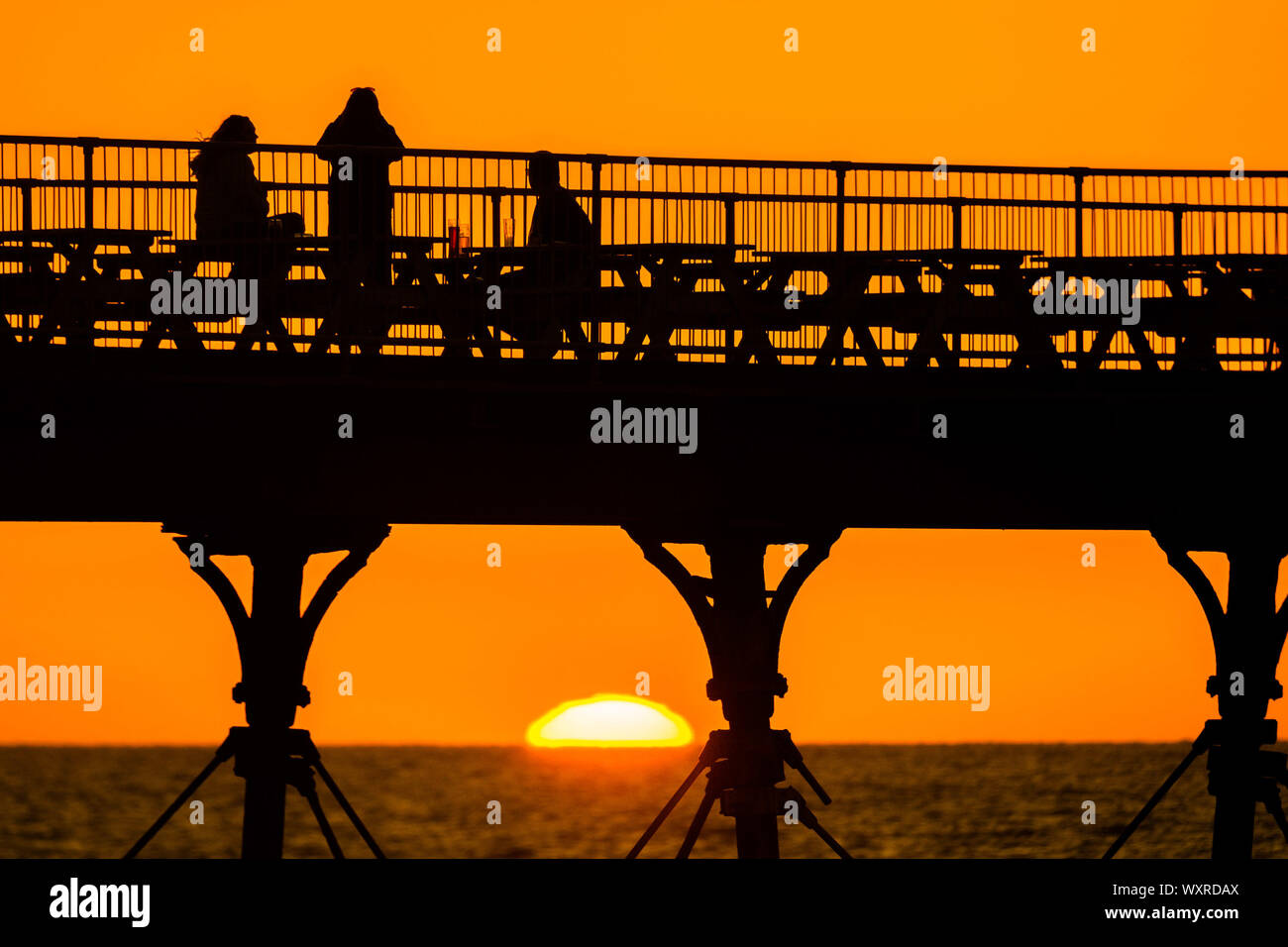 Aberystwyth Wales UK, Tuesday 17 September 2019 People having a drink on Aberystwyth’s Victorian seaside pier are silhouetted as they watch the last  of the sun as it sets over Cardigan Bay, framed by the cast iron legs , on a glorious early autumn evening,  Photo credit Keith Morris / Alamy Live News Stock Photo