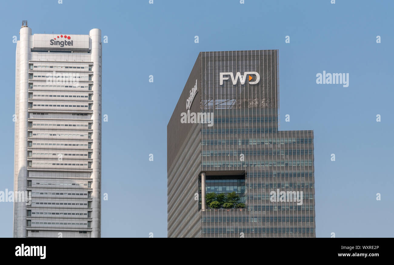 Singapore - March 21, 2019:White  Singtel and dark gray FWD skyscraper towers under blue sky. The latter with green garden halfway up. Stock Photo
