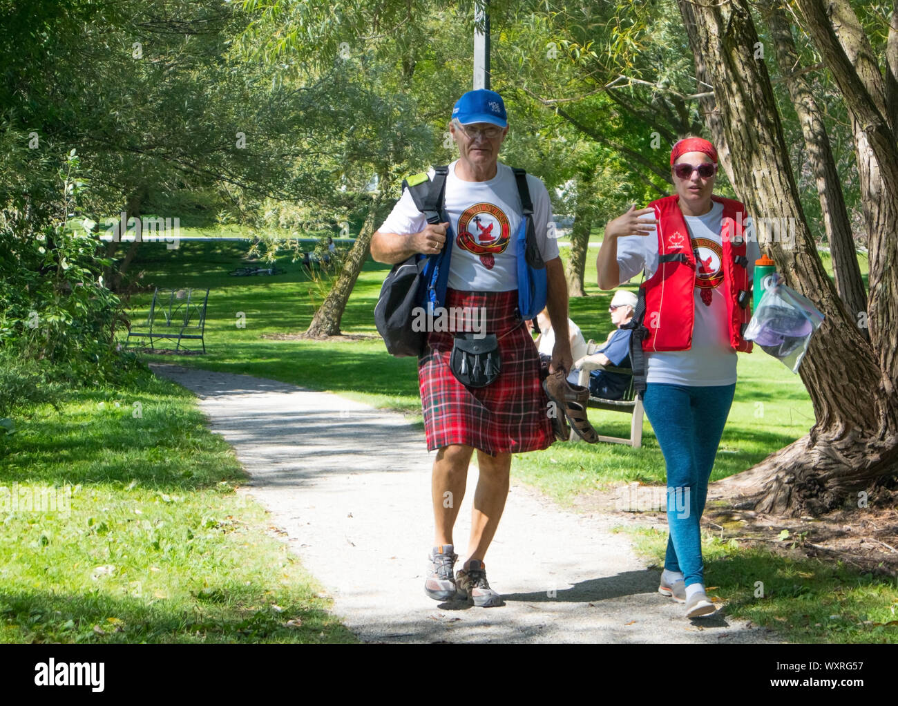 A couple walking thru the park. He wears a traditional Gaelic kilt, she wears a life jacket (the Dragon Boat Festival celebrations 2019).. Stock Photo