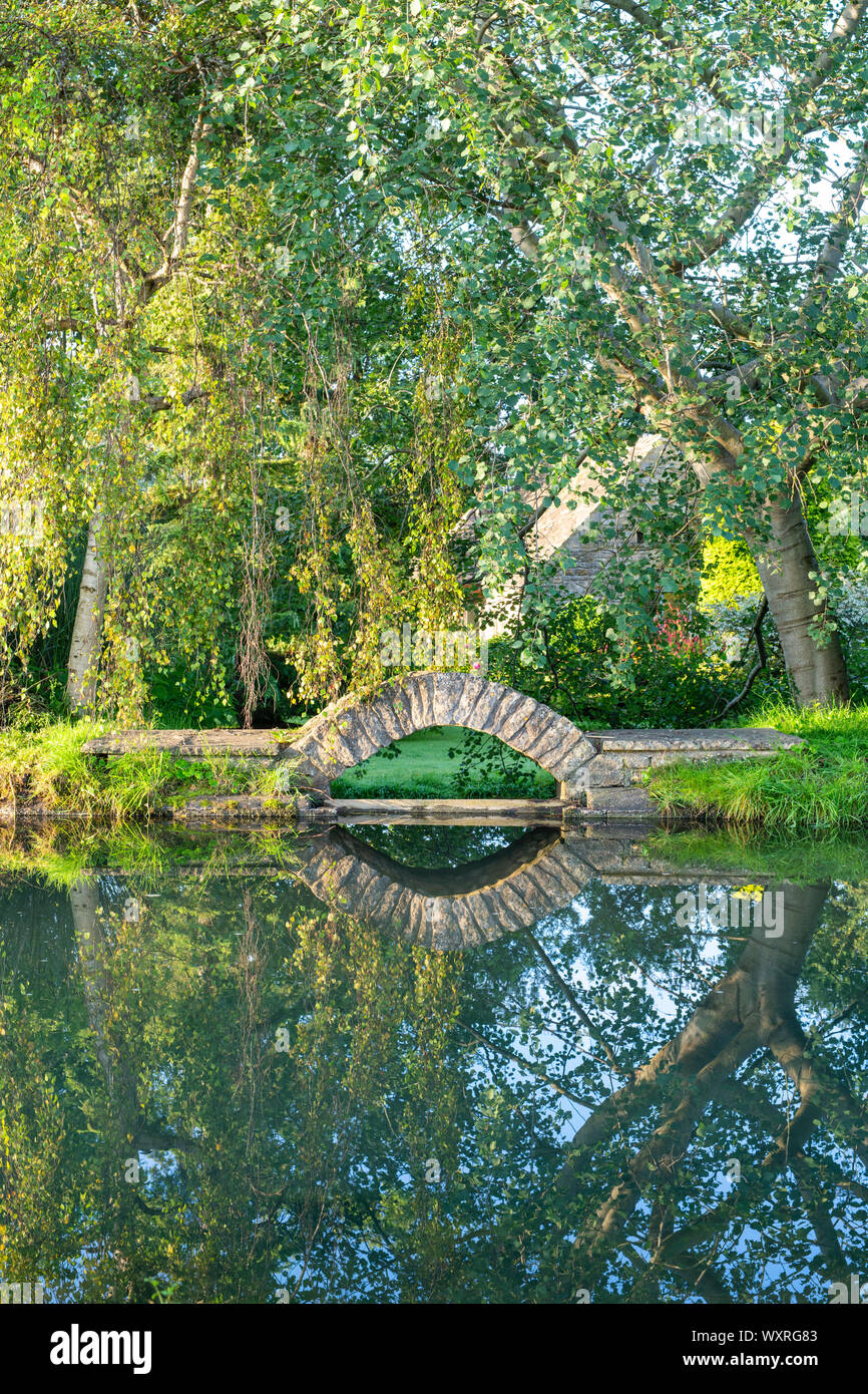Small stone garden bridge on the River Windrush in the early morning sunlight. Bourton on the Water, Cotswolds, Gloucestershire, England Stock Photo