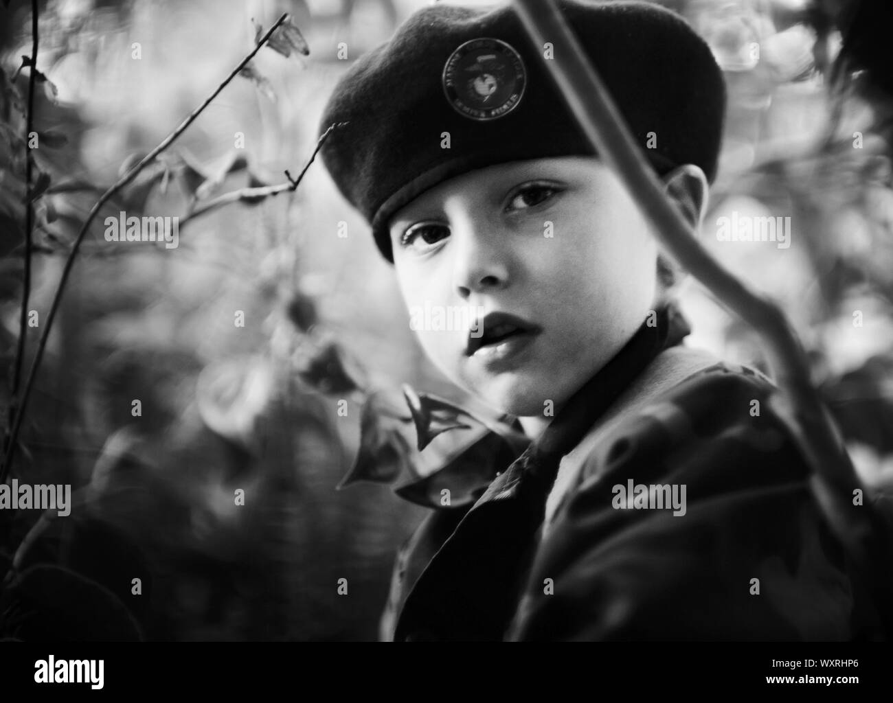 Boy in beret sitting amongst trees Stock Photo