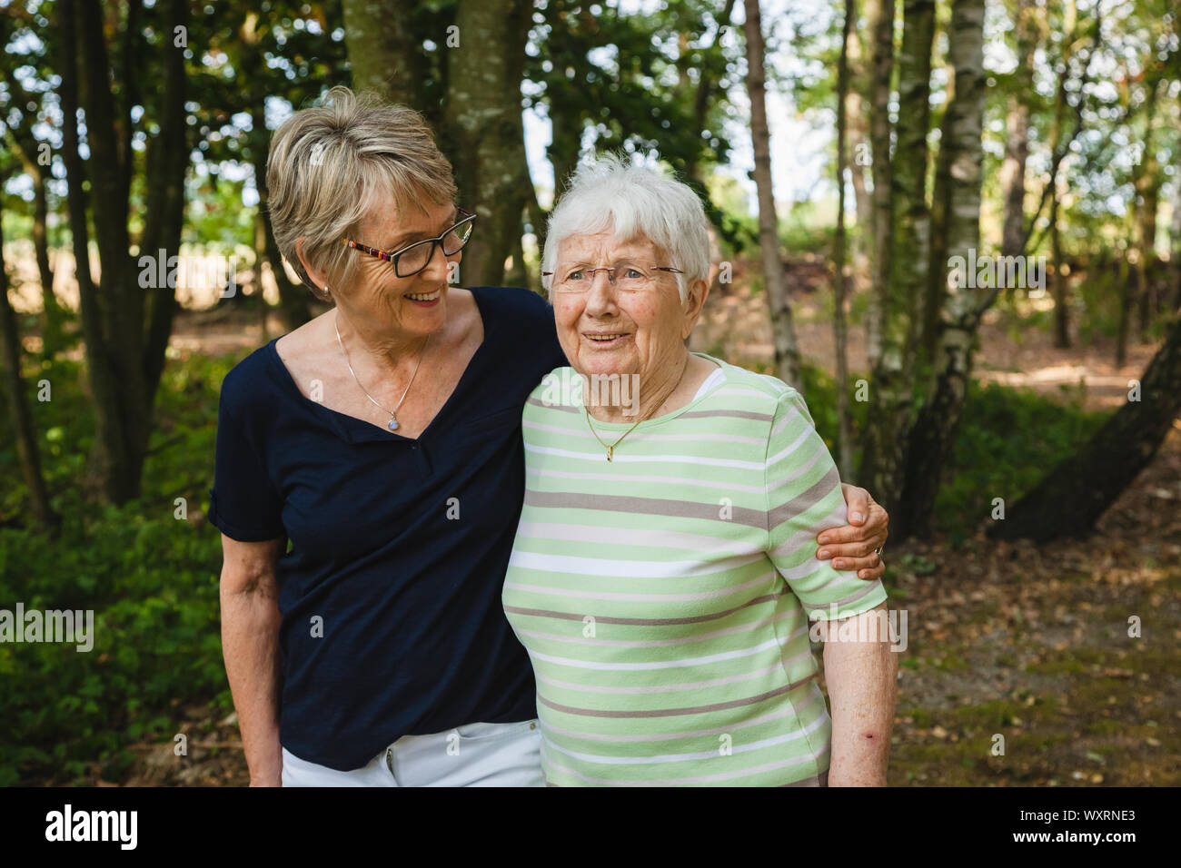Very old joyful senior lady with her daughter walking embraced in a beautiful park, happy for being together Stock Photo