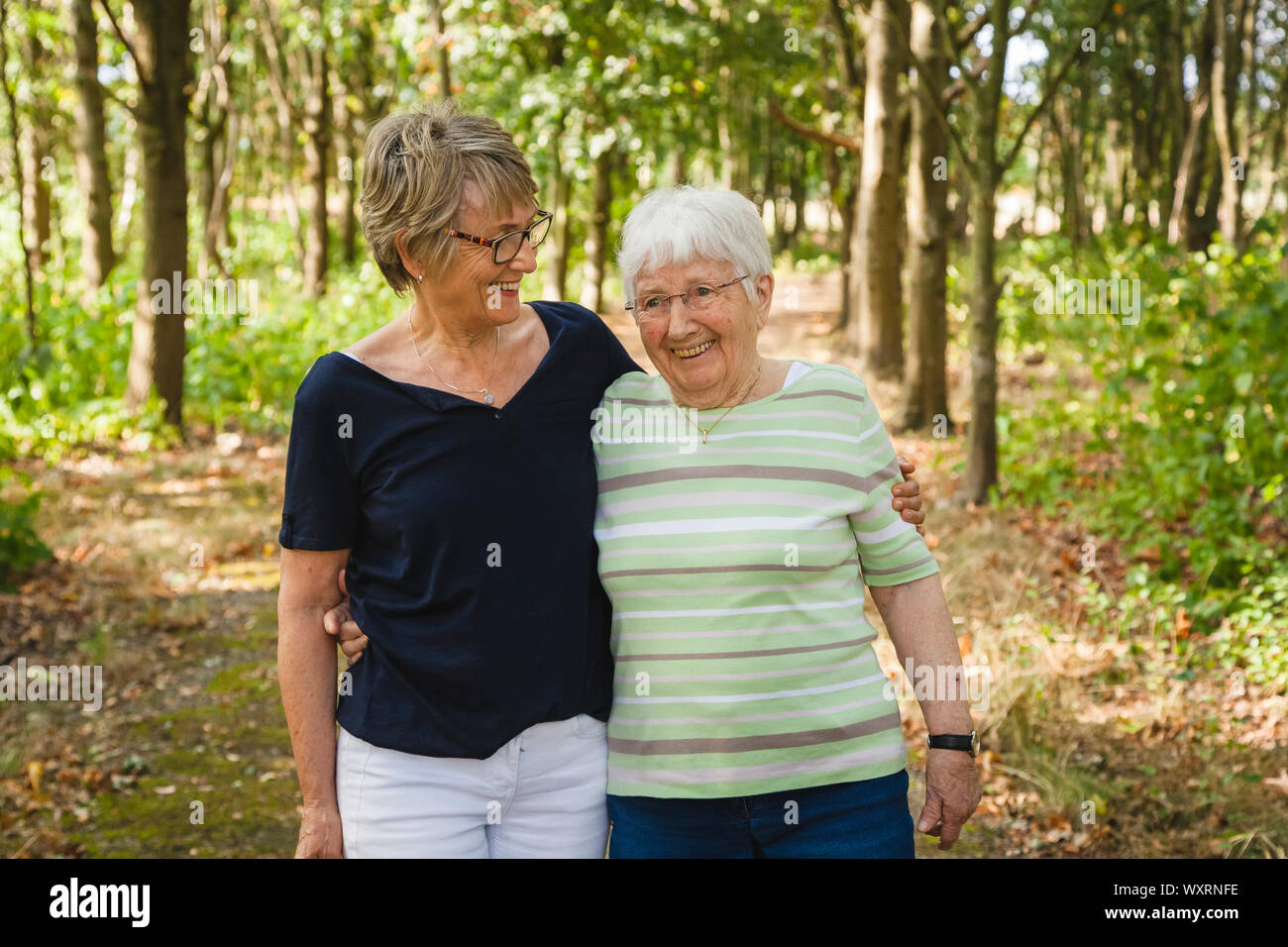 Very old joyful senior lady with her daughter walking embraced in a beautiful park, happy for being together Stock Photo