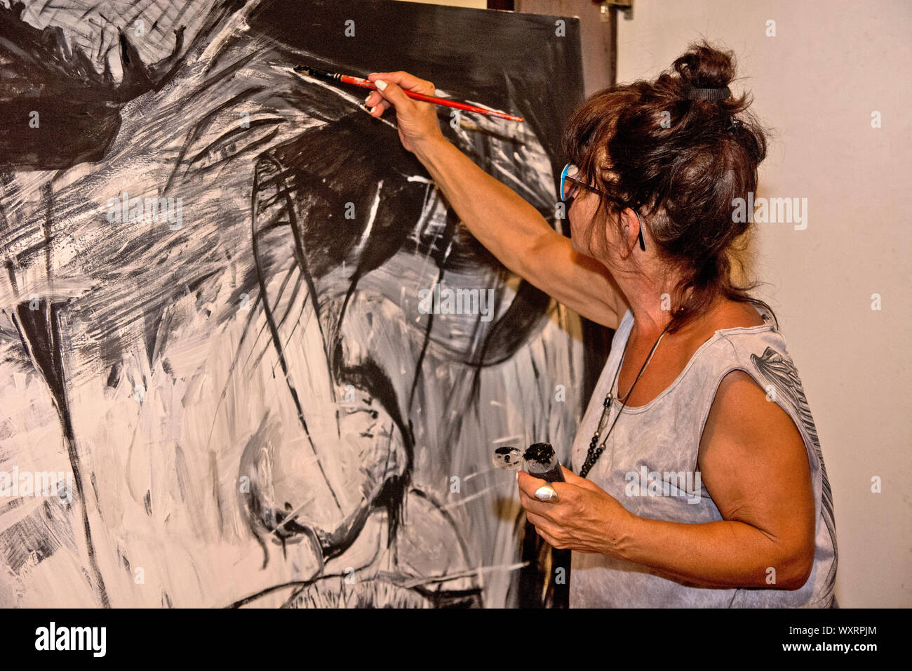 The painter in her studio applies a paint brush to her painting. Stock Photo