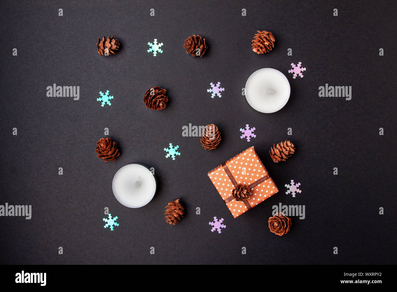 Top view flat lay christmas geometry composition of pine cones, candles, fake snowflakes and small gift box on black background Stock Photo