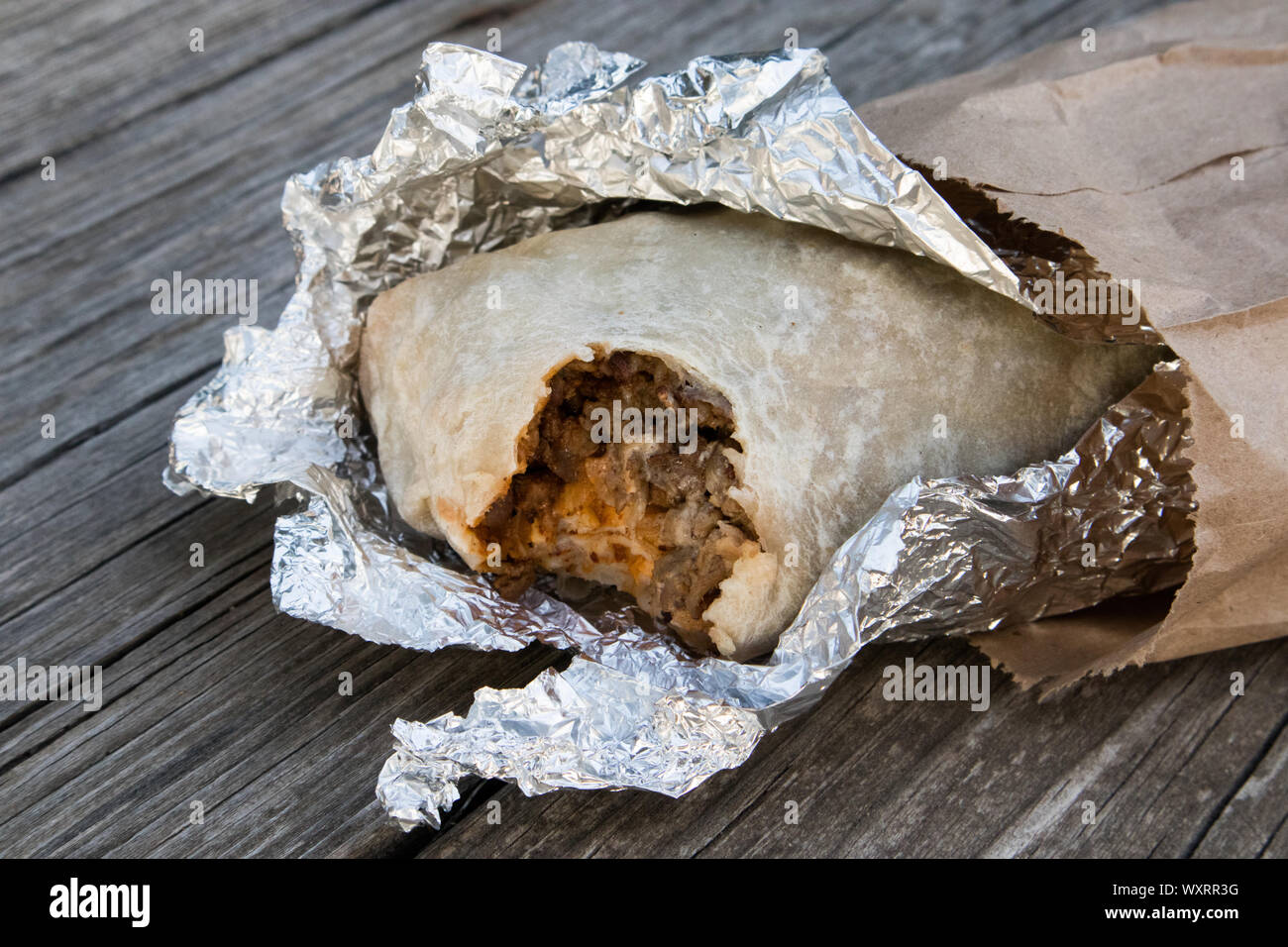 Carne Asada Burrito Wrapped in Foil Open and Paper Bag on Table Stock Photo