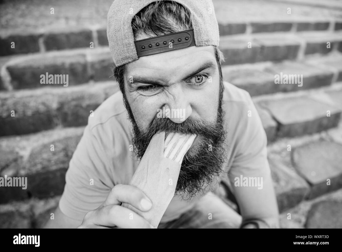 Urban lifestyle nutrition. Junk food. Carefree hipster eat junk food while sit stairs. Guy eating hot dog. Snack for good mood. Unleashed appetite. Street food concept. Man bearded eat tasty sausage. Stock Photo