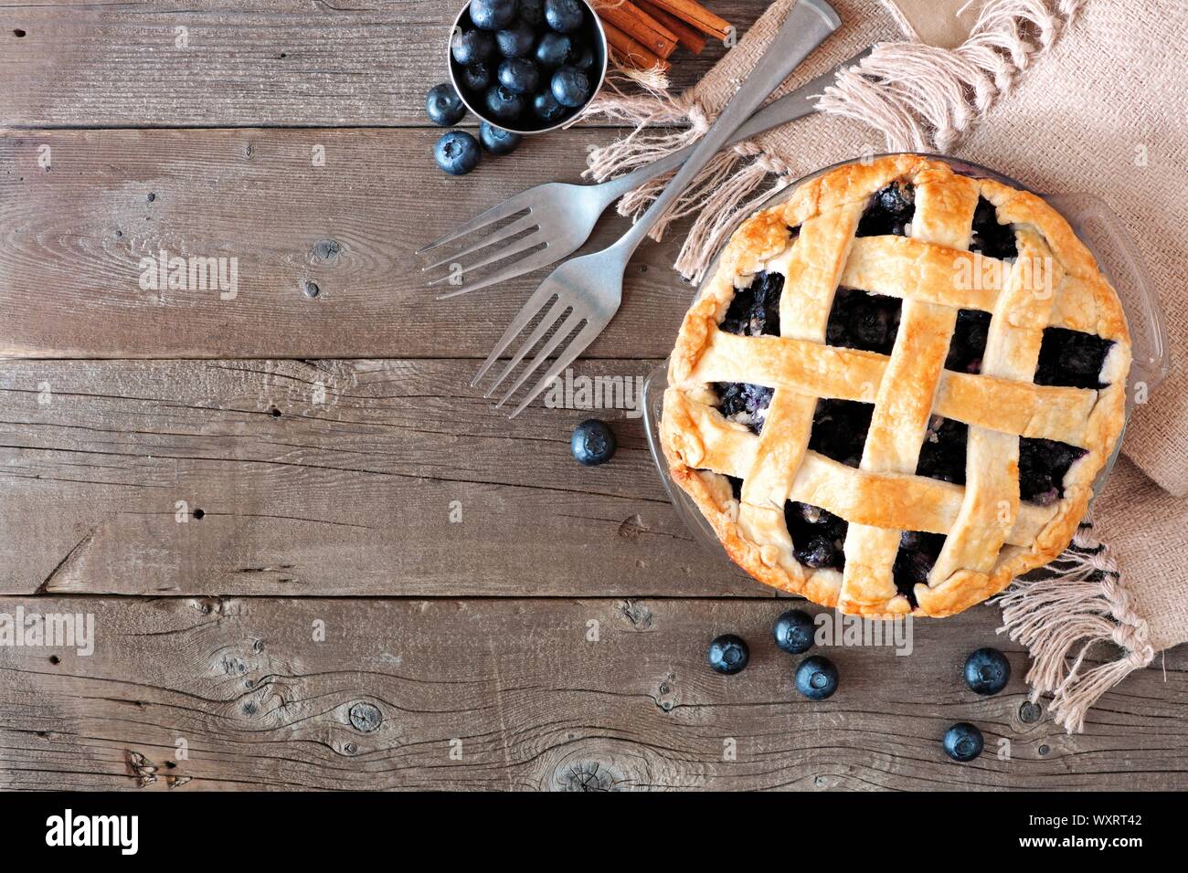 Rustic homemade blueberry pie with lattice pastry. Top view scene. Corner border with copy space over a rustic wood background. Stock Photo