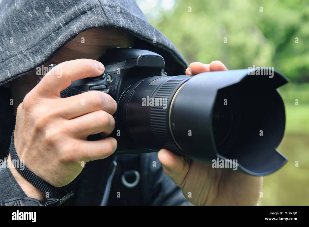 The photographer hidden with the camera. A man in a hood is taking pictures hidden. Stock Photo