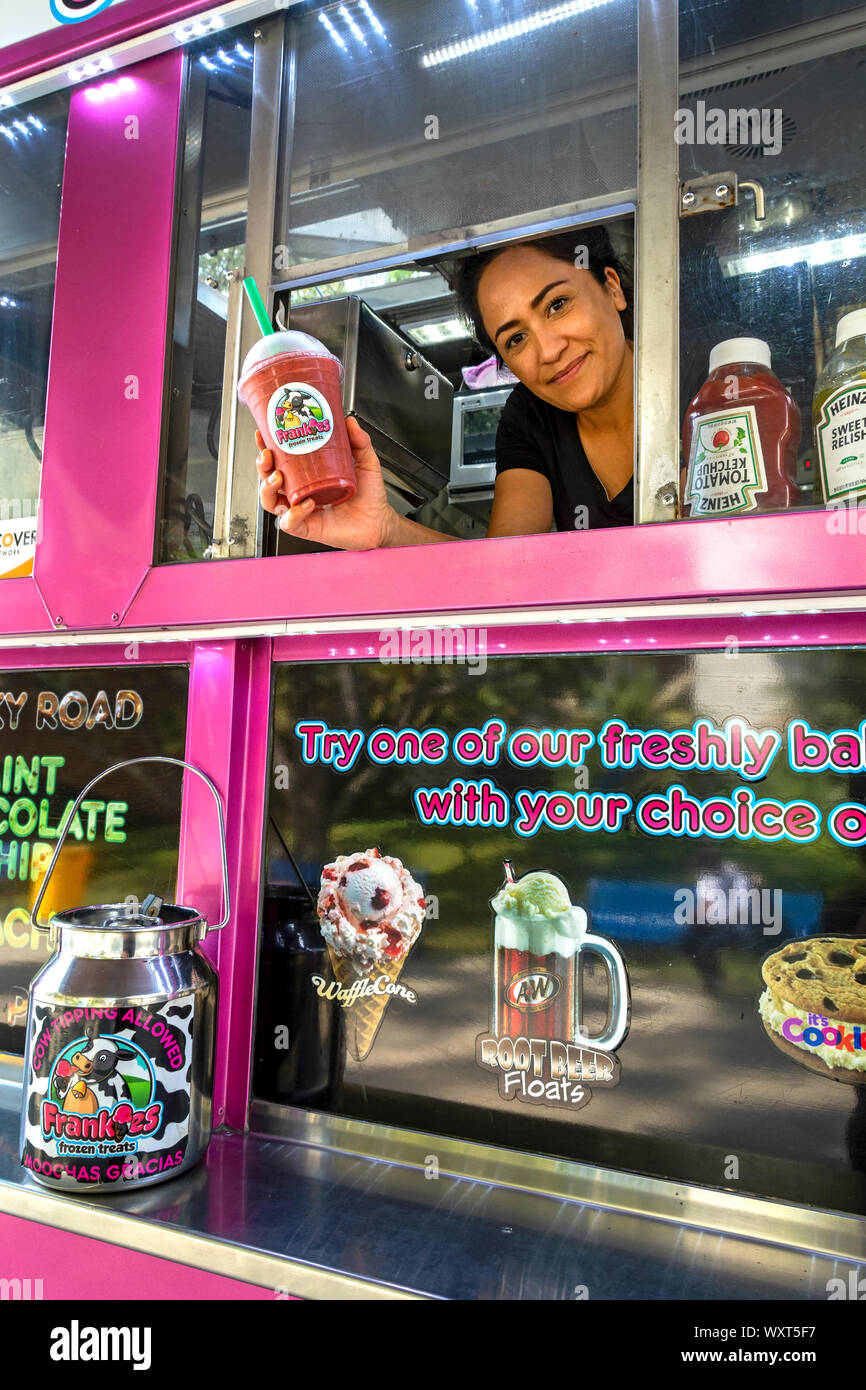 Cypress, CA / USA - Sept. 16, 2019: Attractive food truck waitress holds up one of the frozen drinks that may be purchased at this ice cream truck. Stock Photo