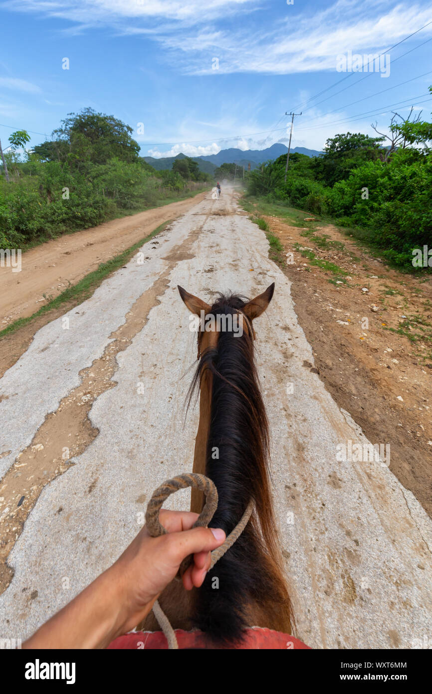 Horseback Riding on a dirty trail in the country side near a small Cuban Town during a vibrant sunny day. Taken in Trinidad, Cuba. Stock Photo