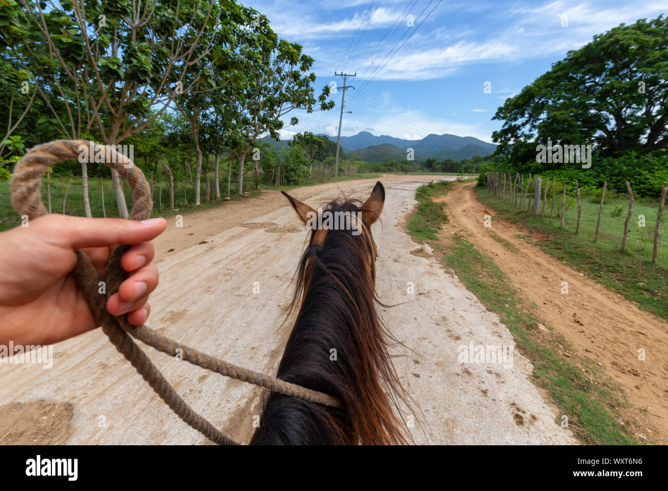 Horseback Riding on a dirty trail in the country side near a small Cuban Town during a vibrant sunny day. Taken in Trinidad, Cuba. Stock Photo